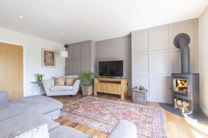 A modern living room with a sofa, TV, fireplace, and decorative rugs. - Beautiful 4 Bed 3 Bath Cotswold Home with Hot Tub (Cheltenham)