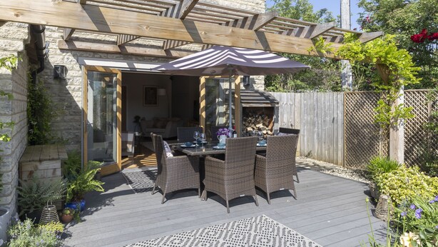 Eine Terrasse mit Korbmöbeln, einem Gartenpergola und einem überdachten Sitzbereich.