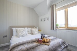 Quarto com cama, bandeja com croissants, cafeteira e janela com vista.
