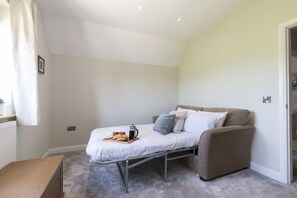 Ein kleines Zimmer mit einem Einzelbett und einer Schlafcouch, einem Heizkörper, einem kleinen Tisch mit einem Tablett Essen und einer Tür zu einem weiteren Raum.