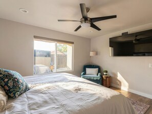 A bedroom with a bed, a chair, a TV, a ceiling fan, and a window. - Saltwater Pool, Billiards, Arcade, Sleeps 12 (San Diego)