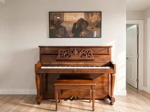 A grand piano with a bench in a room with a white door and a framed picture on the wall. - Saltwater Pool, Billiards, Arcade, Sleeps 12 (San Diego)