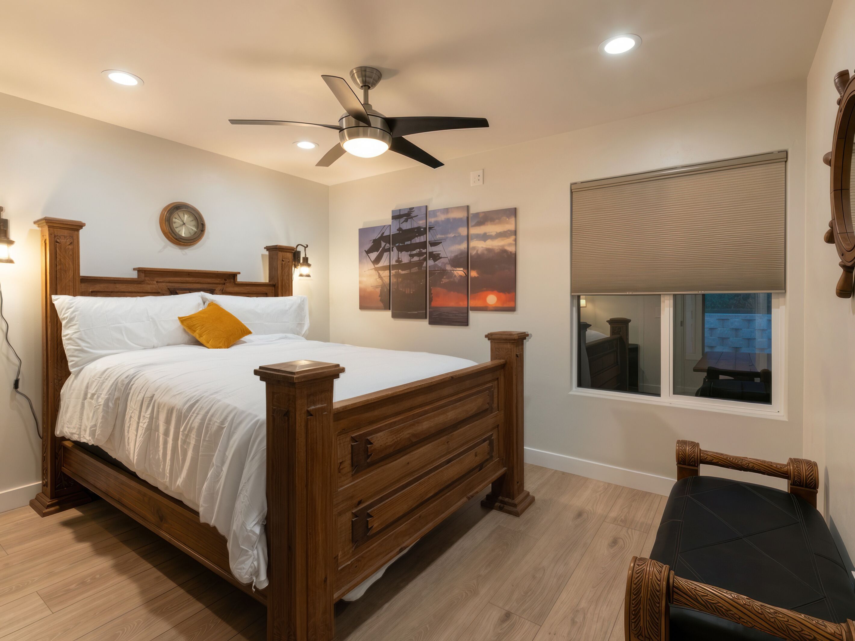 Un dormitorio con cama de madera, ventilador de techo, ventana con persianas y una obra de arte en la pared.
