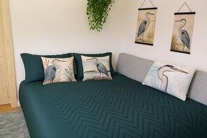 A bed with a dark green chevron-patterned bedspread, three pillows with bird designs, and two wall-mounted bird paintings.