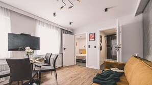 Ein modernes Wohnzimmer mit einer Couch, einem Esstisch mit Stühlen, einem Fernseher und einem Bett im Hintergrund.