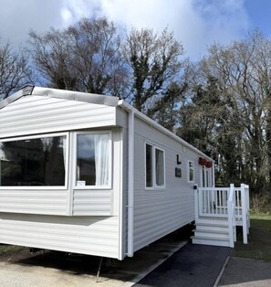 Een witte stacaravan met een veranda en een trap erheen.