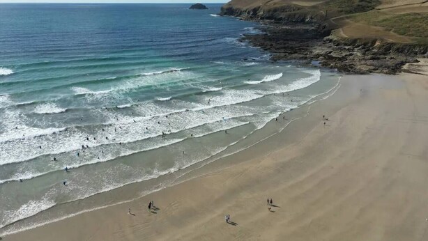 A coastal beach with waves, a sandy shore, and a distant rocky outcrop.