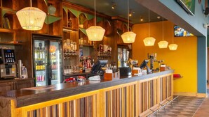 A bar area with a wooden counter, hanging lights, and a variety of bottles and glasses.
