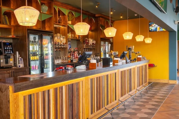 A bar area with a wooden counter, hanging lights, and a variety of bottles and glasses.