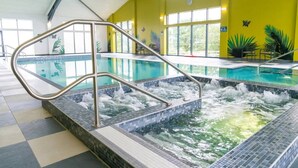 An indoor pool with a hot tub, metal handrails, and a yellow wall with plant decorations.