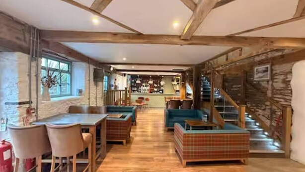 Amplia habitación con techo de madera, comedor con mesa y sillas, sofá y escalera que sube a un nivel superior.