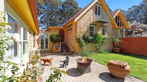 Una casa de piedra con un patio de ladrillo, un brasero y dos perros.