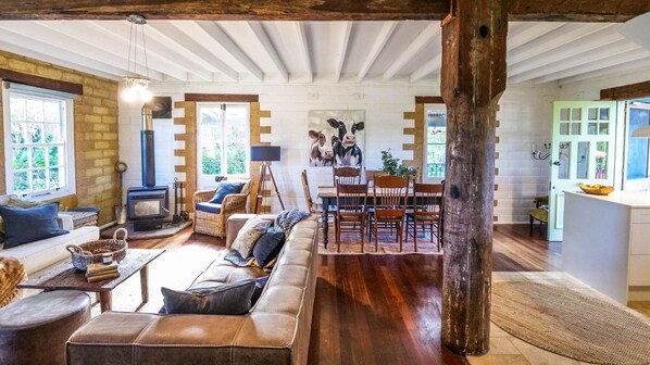 A rustic interior with a fireplace, seating area, dining table, and a painting of cows.