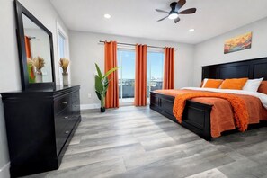 A modern bedroom with a bed, a dresser, a ceiling fan, and a large window with curtains. - New Luxury Beach House, Rooftop Terrace, Ocean Views, Walk to Beach (Seaside Heights)