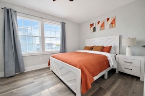 A bedroom with a bed, a nightstand, a lamp, and a window with curtains. - New Luxury Beach House, Rooftop Terrace, Ocean Views, Walk to Beach (Seaside Heights)