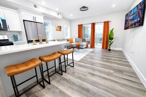 A modern kitchen with a built-in refrigerator, a bar area with stools, and a dining area with a sofa and table. - New Luxury Beach House, Rooftop Terrace, Ocean Views, Walk to Beach (Seaside Heights)