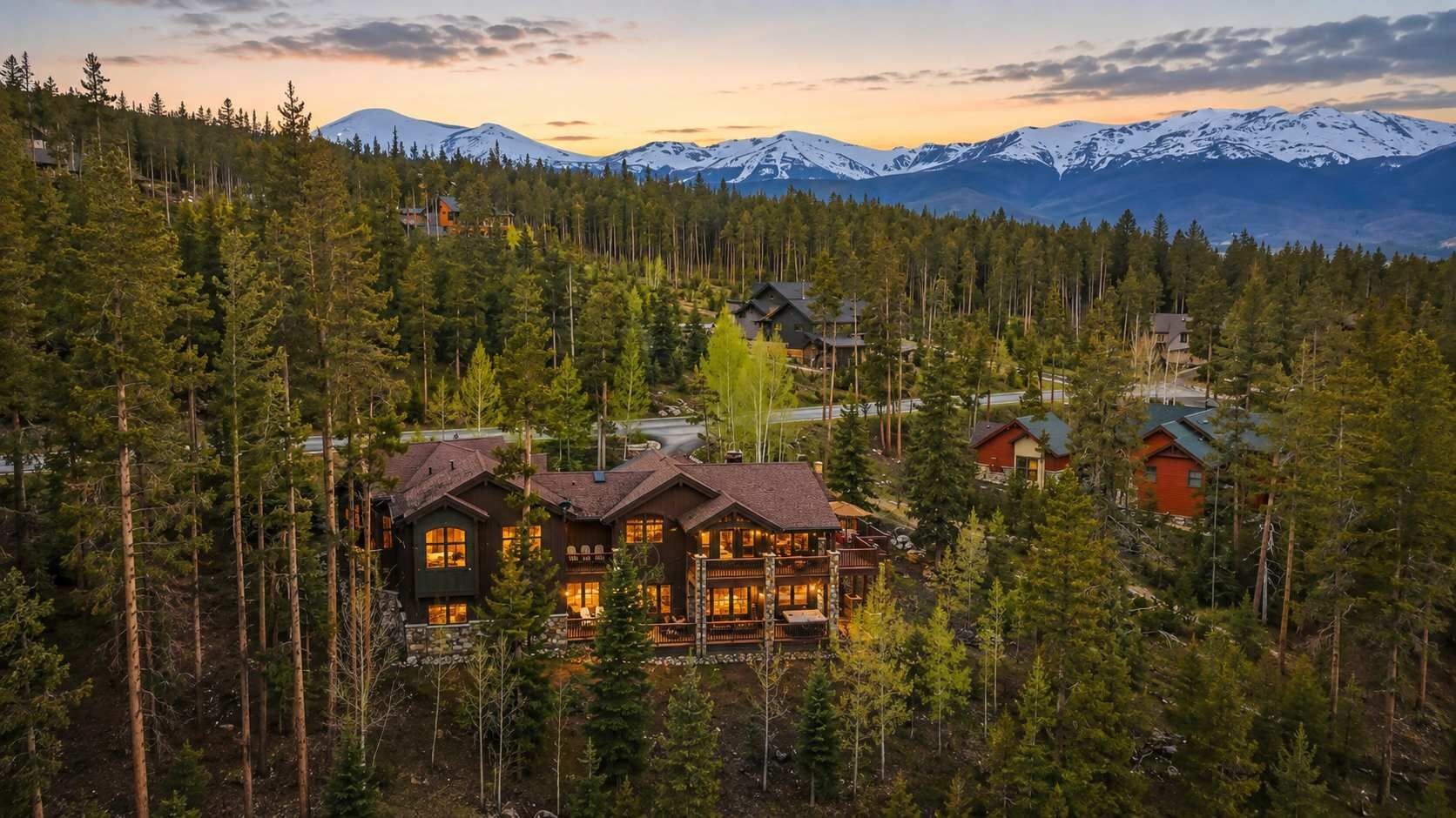 A lodge with multiple cabins surrounded by dense forest and mountains in the background.