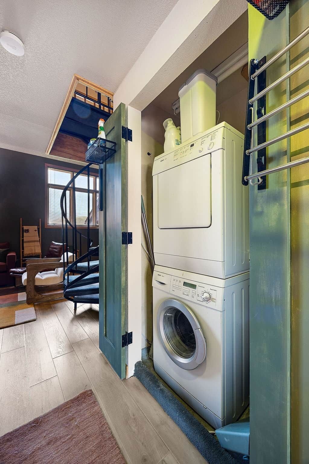 A compact laundry room with a front-loading washing machine, a drying rack, and a small window.