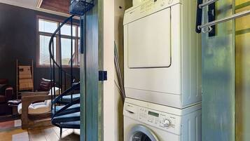 A compact laundry room with a front-loading washing machine, a drying rack, and a small window.