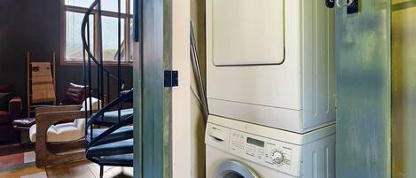 A compact laundry room with a front-loading washing machine, a drying rack, and a small window.