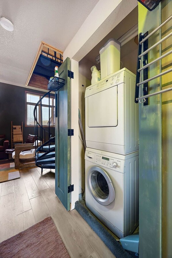 A compact laundry room with a front-loading washing machine, a drying rack, and a small window.