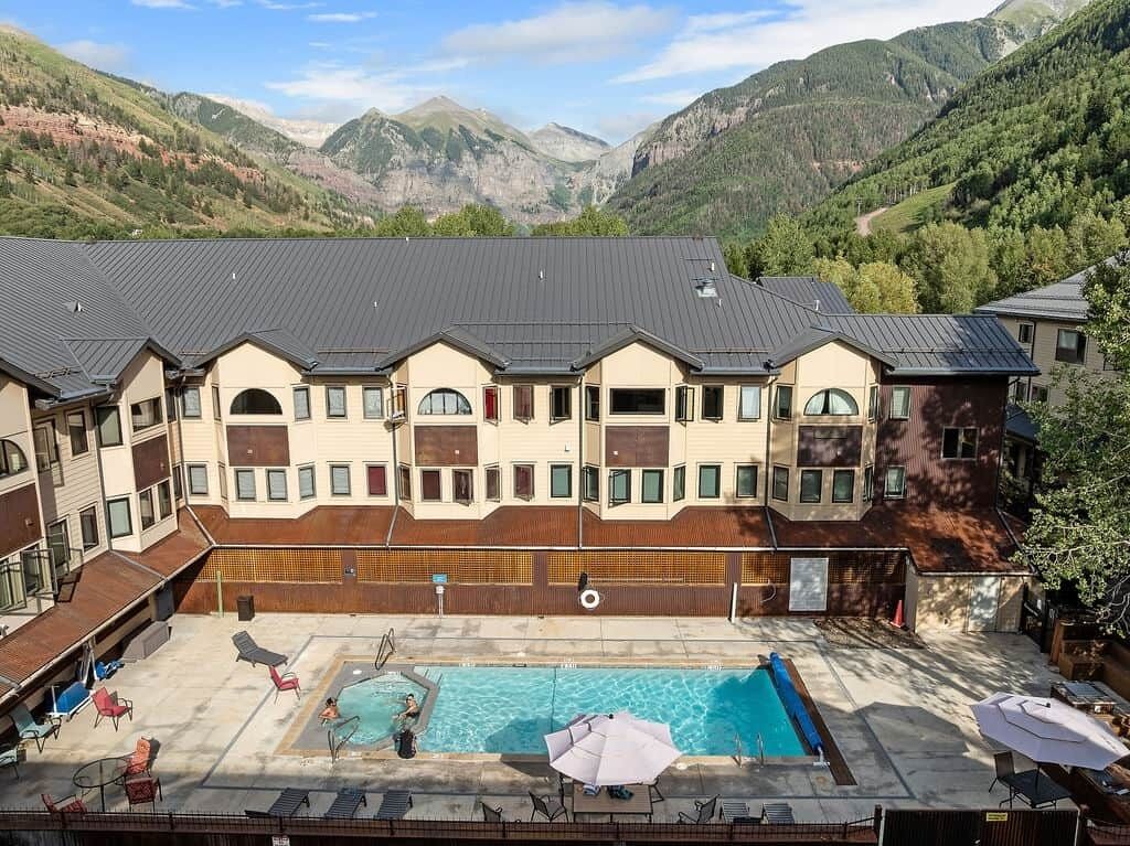 A hotel with a swimming pool, outdoor seating, and a view of mountains.