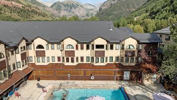 A hotel with a swimming pool, outdoor seating, and a view of mountains.