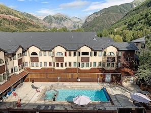 A hotel with a swimming pool, outdoor seating, and a view of mountains.