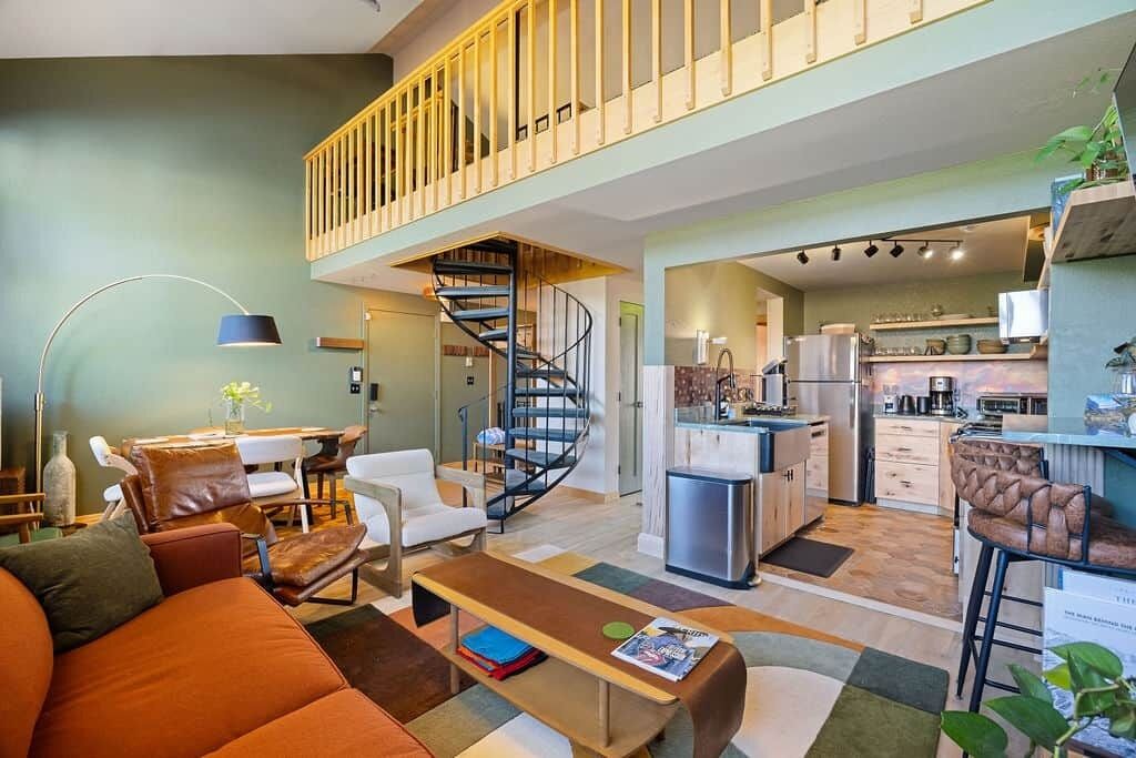 A modern apartment with a living room, dining area, kitchen, and a staircase leading to an upper floor.
