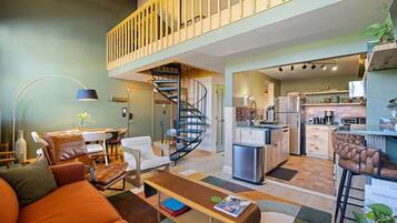 A modern apartment with a living room, dining area, kitchen, and a staircase leading to an upper floor.