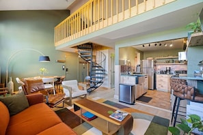 A modern apartment with a living room, dining area, kitchen, and a staircase leading to an upper floor.
