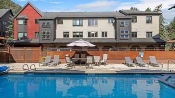 A two-story building with a swimming pool, outdoor seating, and a mountain backdrop.