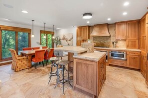 A modern kitchen with wooden cabinets, a central island, and a dining area with orange chairs. - Ski, Hike & Unwind — Heart of Telluride — 3bd/3ba (Telluride)