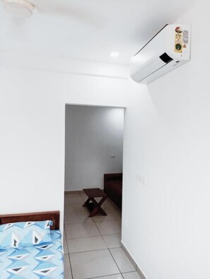 A room with a bed, a small table, and an air conditioning unit mounted on the wall.