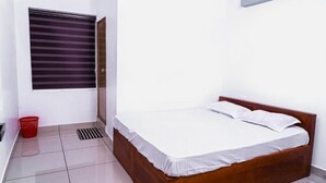 Quarto com cama de madeira, roupa de cama branca, janela com persianas, um cesto vermelho e chão revestido de azulejos.