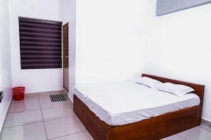 A bedroom with a wooden bed, white bedding, a window with blinds, a red basket, and a tiled floor.