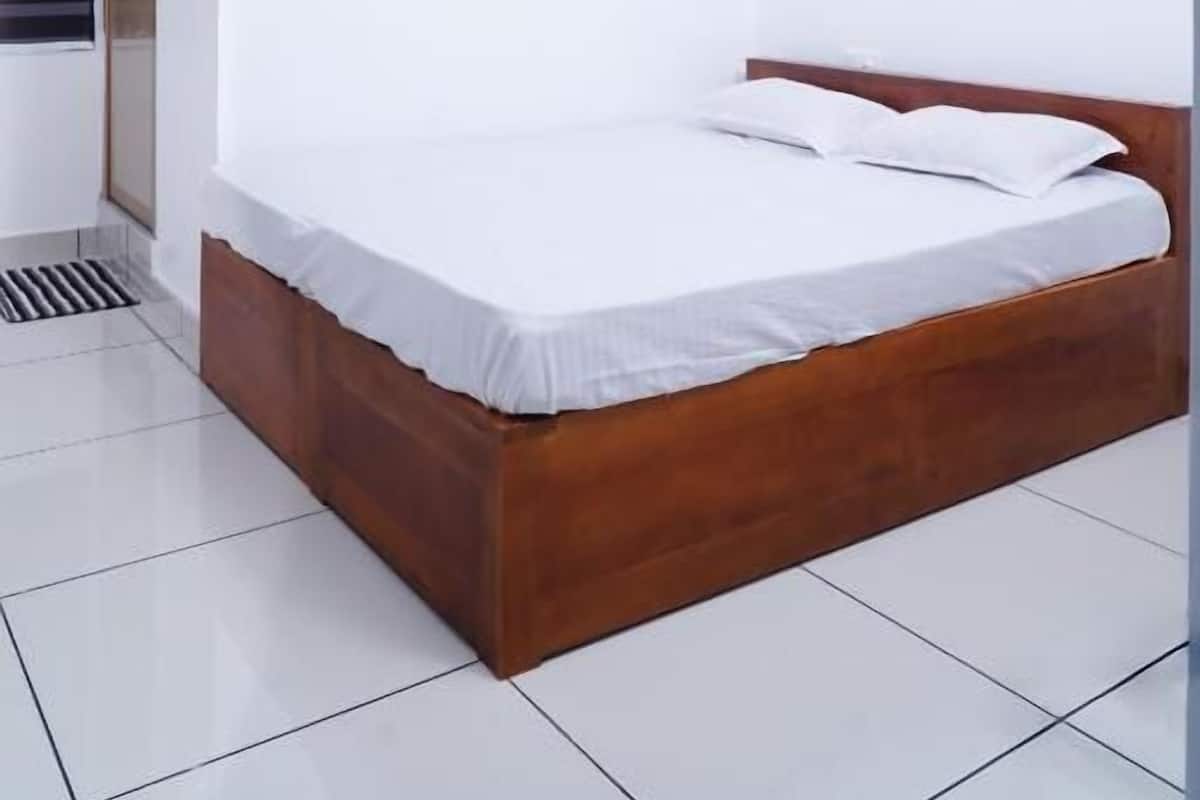 Un dormitorio con una cama de madera, ropa de cama blanca, un ventilador de techo y una ventilación a la izquierda.