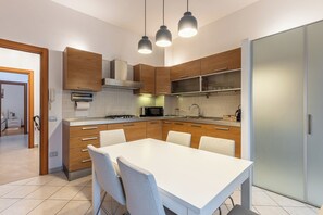 Una cocina moderna con armarios de madera, encimera blanca y un comedor con mesa y sillas blancas.