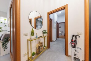 Een gang met een spiegel, een console tafel met planten en een deur die naar een andere kamer leidt.