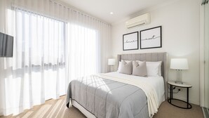 A modern bedroom with a large bed, two bedside lamps, a flat-screen TV, and a wall-mounted air conditioner. - Pet Friendly - The Viewpoint, Port Melbourne (Port Melbourne)