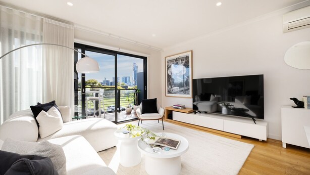 A modern living room with a large TV, a sofa, a coffee table, and a balcony with a city view. - Pet Friendly - The Viewpoint, Port Melbourne (Port Melbourne)