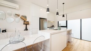 A modern kitchen with white cabinetry, a central island, pendant lighting, and a view of the city. - Pet Friendly - The Viewpoint, Port Melbourne (Port Melbourne)