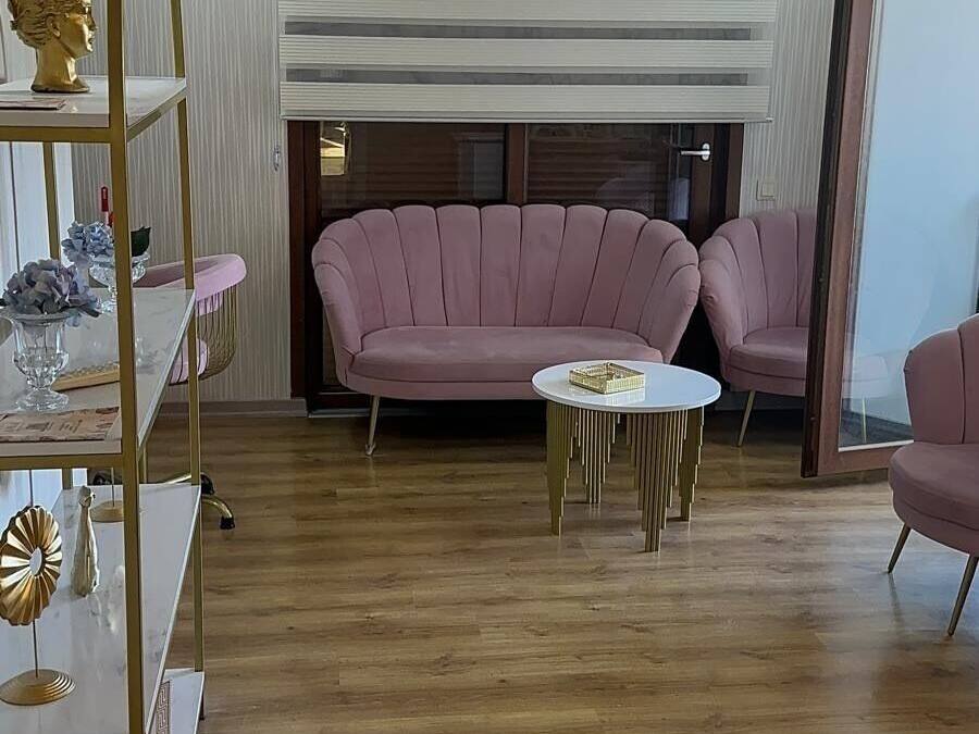 Un salón con piso de madera, un sofá rosa, una mesa de centro redonda y una estantería con marco dorado.