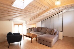 Ein Loft-Zimmer mit Holzbalkendecke, einer Couch, einem Sessel und einem kleinen Tisch.