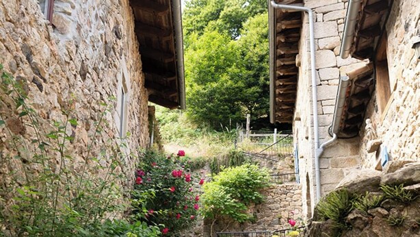 Un étroit sentier de pierre, bordé de bâtiments rustiques en pierre avec des poutres en bois, mène à un escalier.