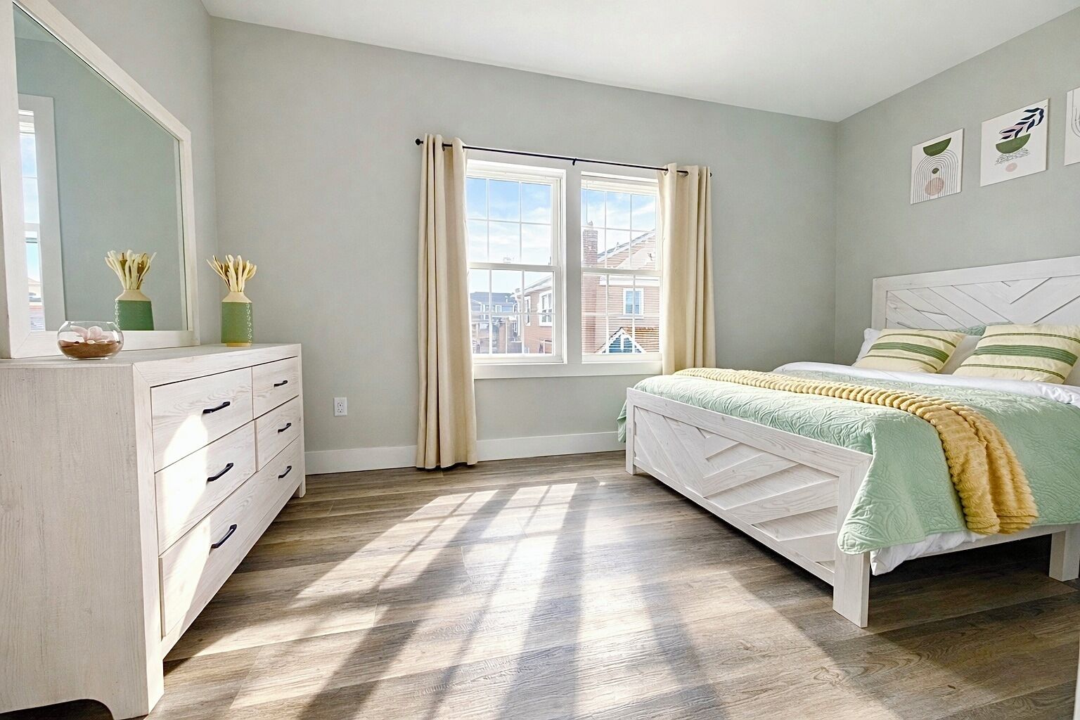 A bedroom with a bed, a dresser, a window, and artwork on the wall.