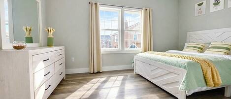 A bedroom with a bed, a dresser, a window, and artwork on the wall.