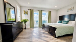 A bedroom with a large bed, a dresser, a potted plant, and a view of the outdoors. - Luxury Beach House, Rooftop Deck, Ocean Views, Walk to Beach & Boardwalk (Seaside Heights)