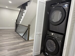 A laundry room with two stacked washers and dryers, a wooden staircase, and a grey herringbone floor. - Luxury Beach House, Rooftop Deck, Ocean Views, Walk to Beach & Boardwalk (Seaside Heights)