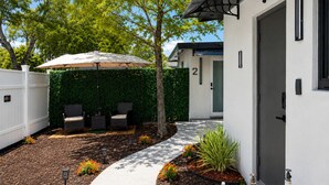 Un patio con mobiliario exterior, una valla blanca y un seto.